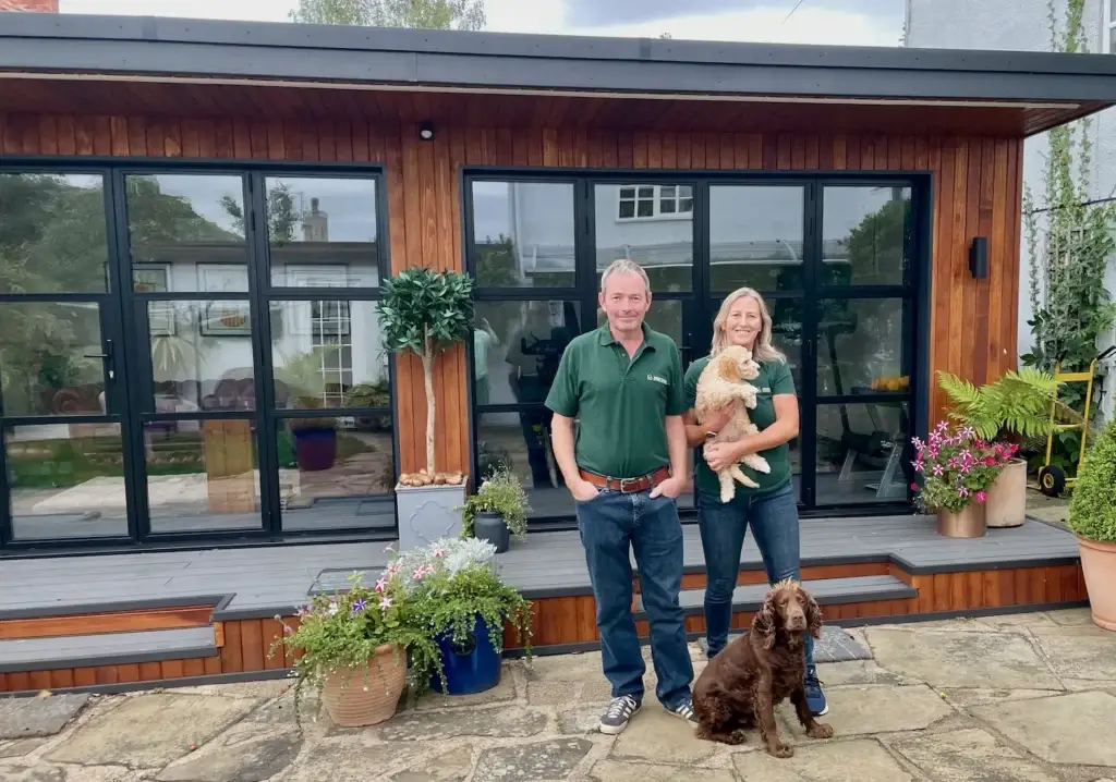 2 people standing infront of a cedar clad Garden Room with Heritage style doors